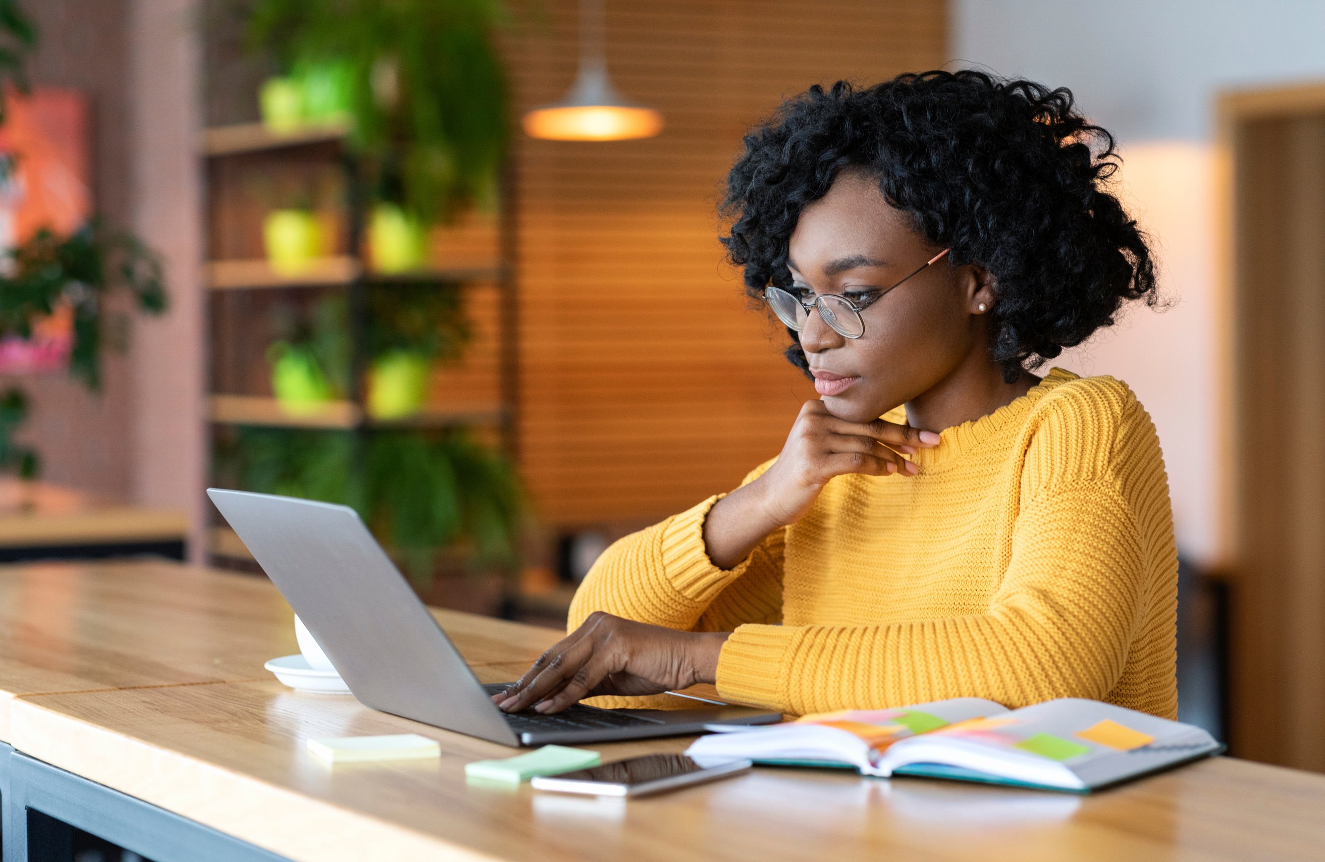 Black girl working in cafe, browsing on laptop